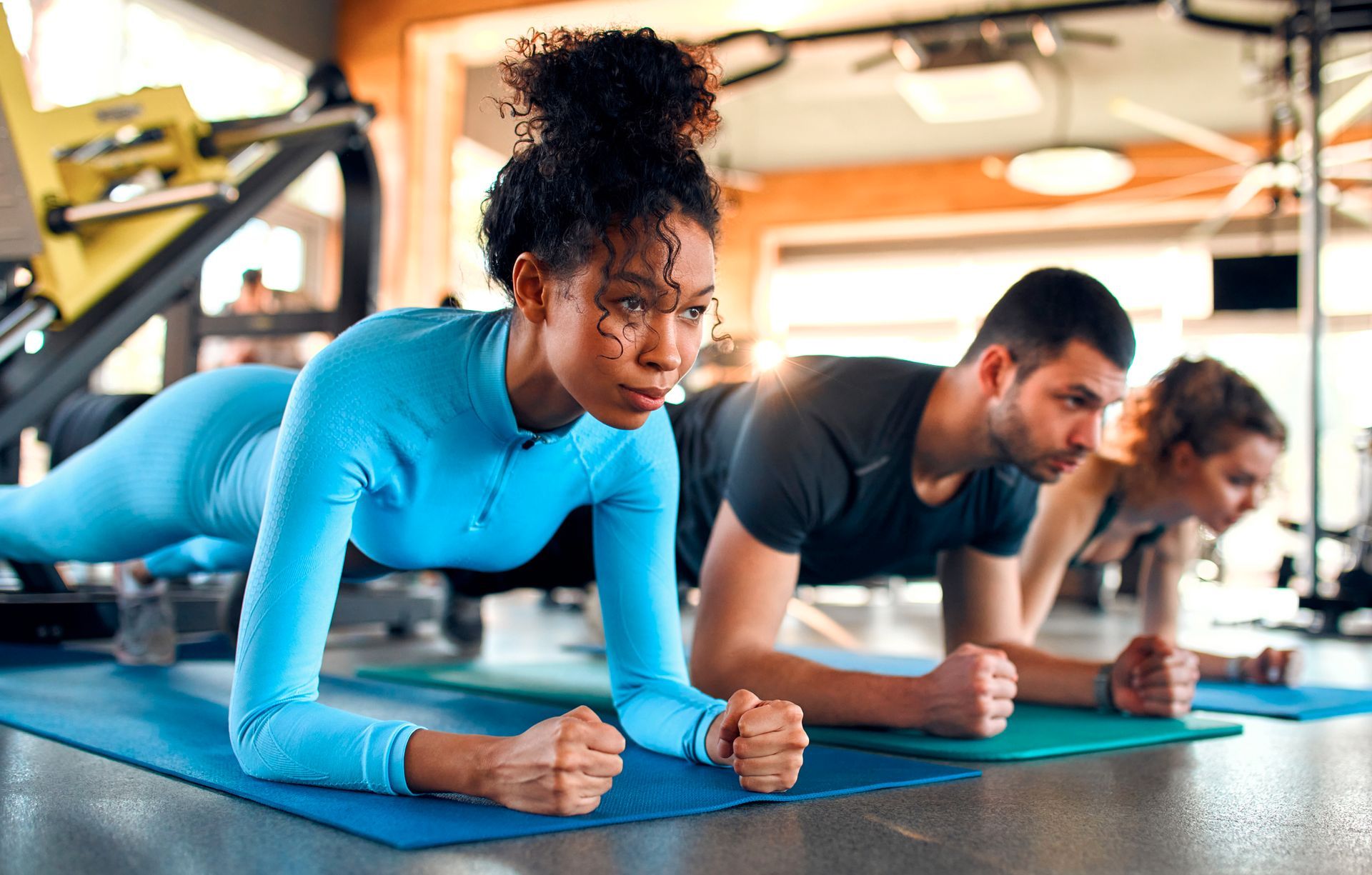 A group of people are doing plank exercises on yoga mats in a gym.