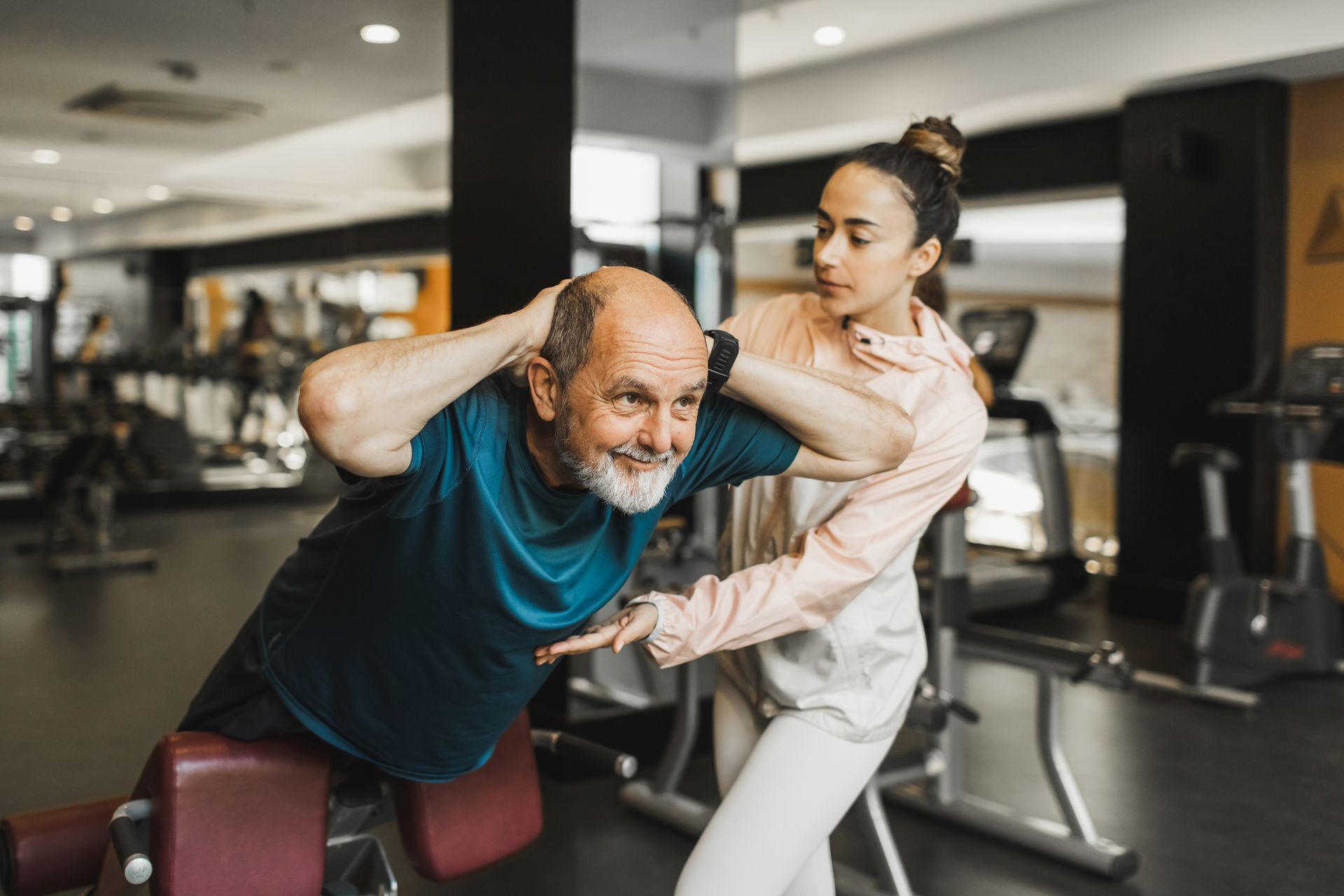 A woman is helping an older man do exercises in a gym.
