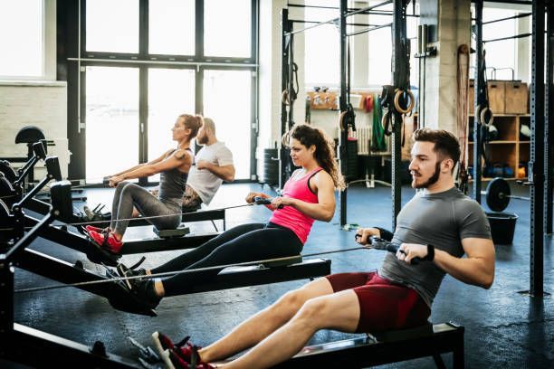 A group of people are rowing machines in a gym.