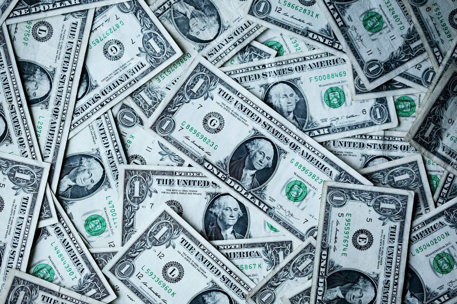 A close-up image showing a scattered pile of United States one-dollar bills, featuring the