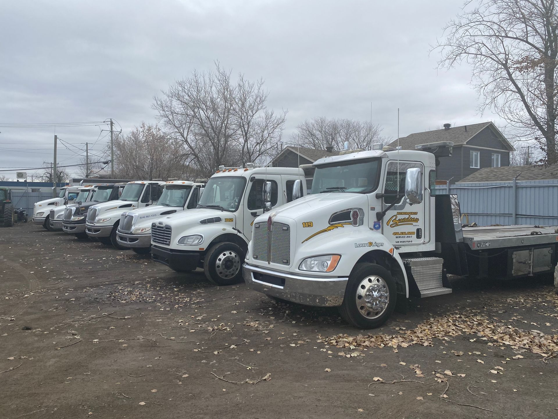 Une rangée de dépanneuses blanches garées sur un terrain par une journée nuageuse.