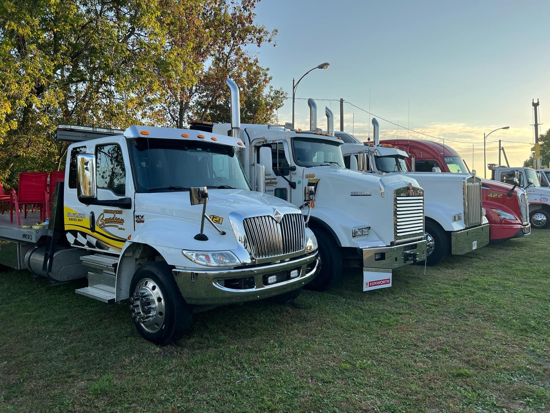 Rangée de dépanneuses garées sur l'herbe sous un ciel partiellement nuageux. Couleurs variées : blanc, rouge et argent.