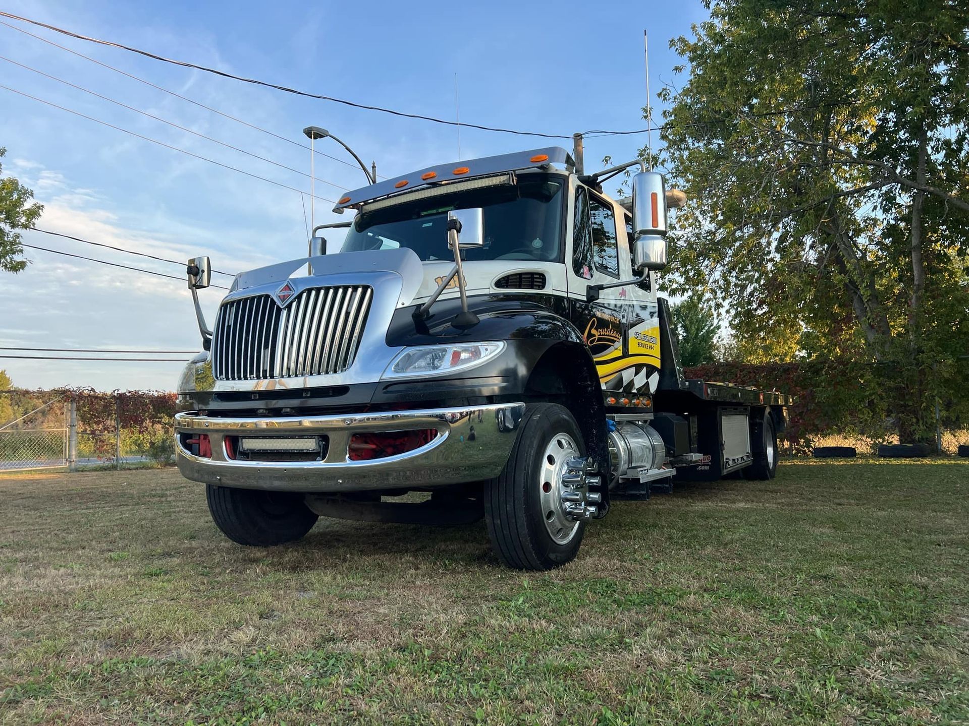 Une dépanneuse garée sur une pelouse. Le véhicule est noir et argent avec des touches de chrome sous un ciel bleu.