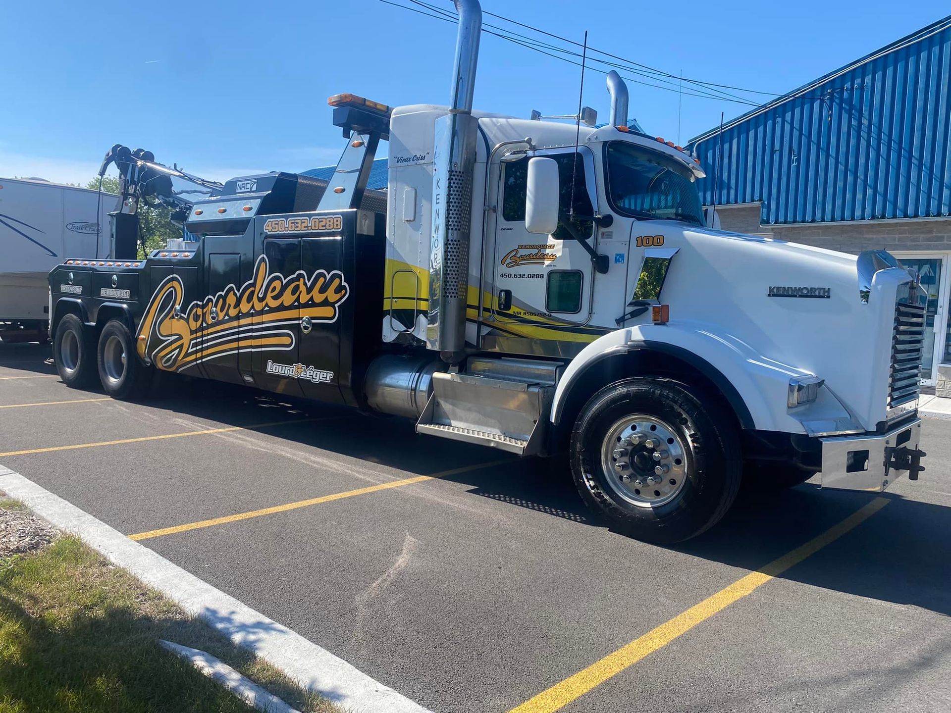 Une dépanneuse blanche et noire avec des accents jaunes garée sur un terrain pavé par une journée ensoleillée.
