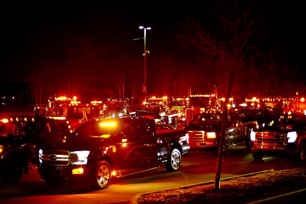 Un grand rassemblement de camions et de véhicules la nuit avec des feux d'urgence clignotants, créant une lueur rouge et orange.