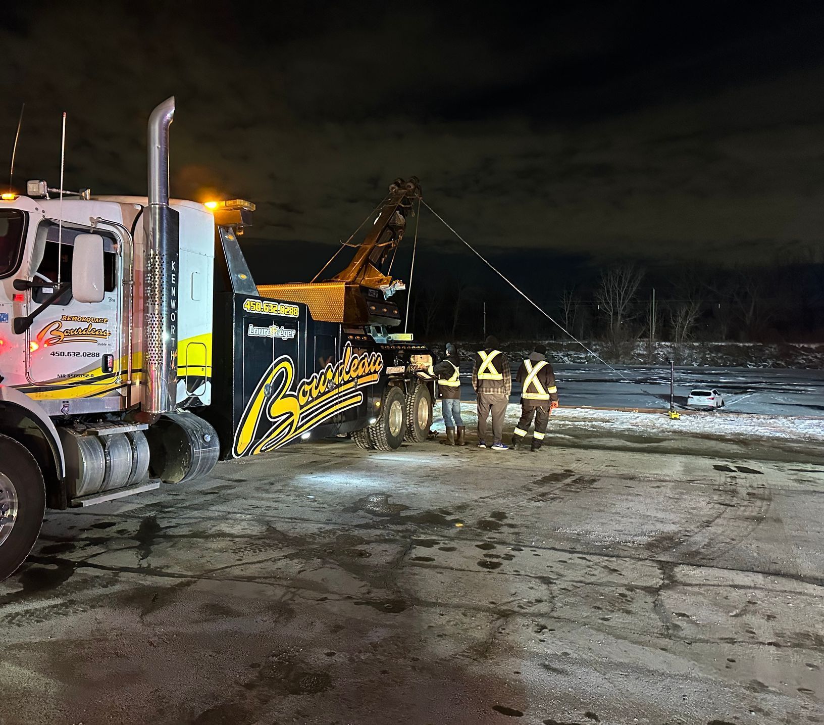Dépanneuse de nuit avec personnel d'urgence, récupérant éventuellement un véhicule sur un terrain enneigé.