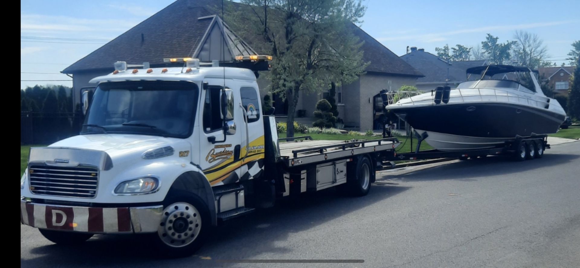 Une dépanneuse transportant un bateau sur une remorque dans une rue résidentielle.