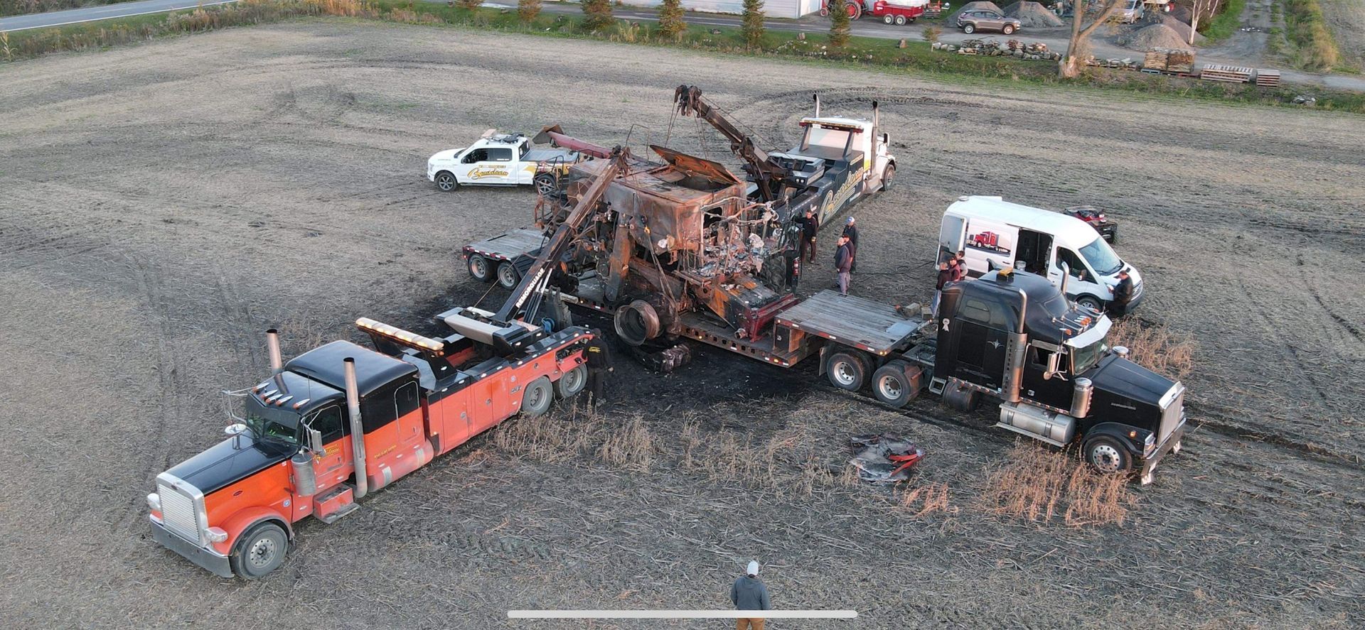 Vue aérienne de plusieurs dépanneuses entourant un véhicule gravement endommagé dans un champ. La scène semble être celle d'un accident.