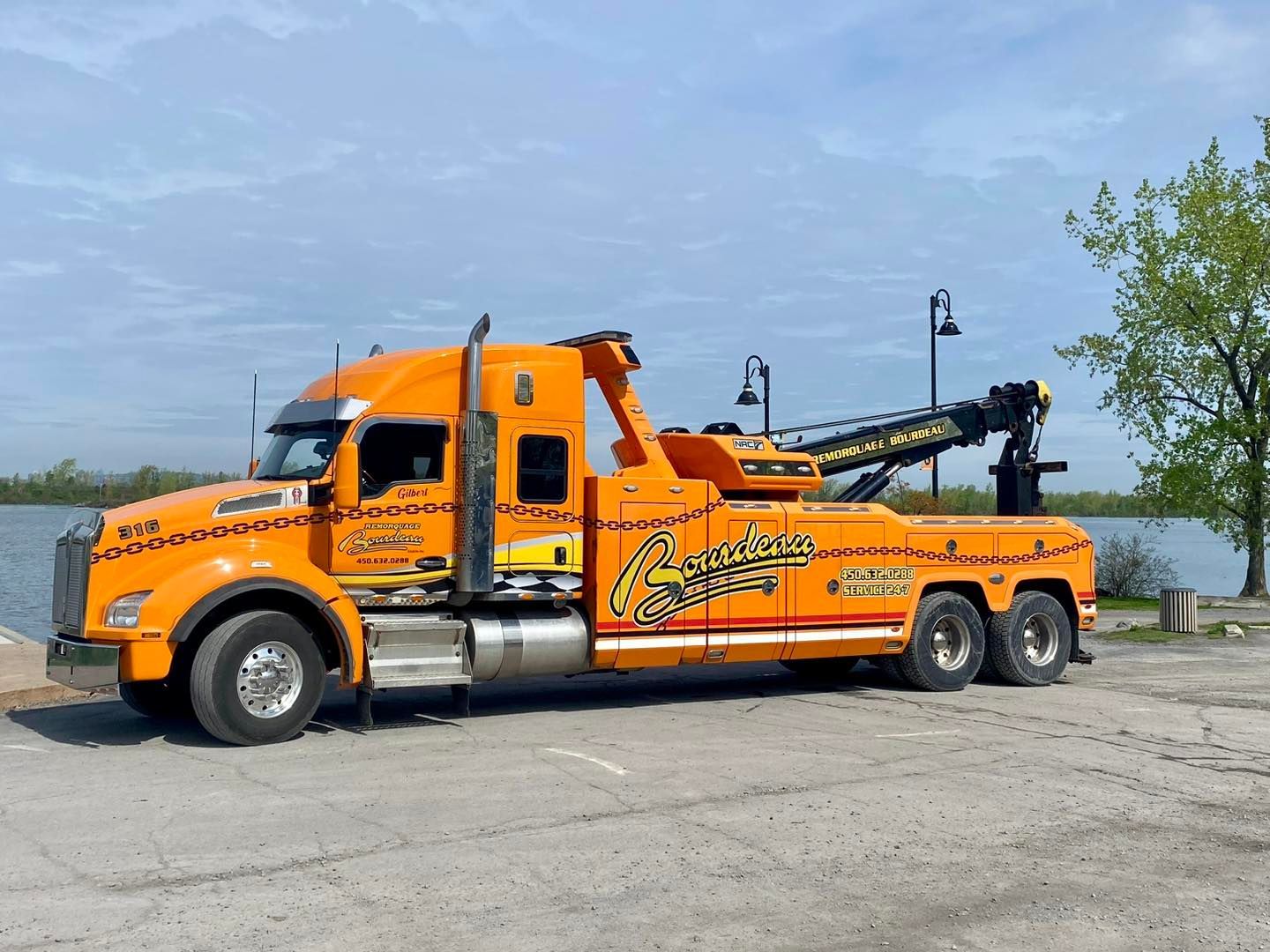 Dépanneuse orange garée près d'un plan d'eau, probablement un lac. 