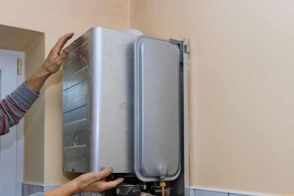 A person is installing a boiler on a wall.