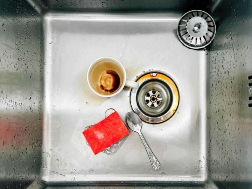 A dirty kitchen sink with a cup , spoon , and sponge.