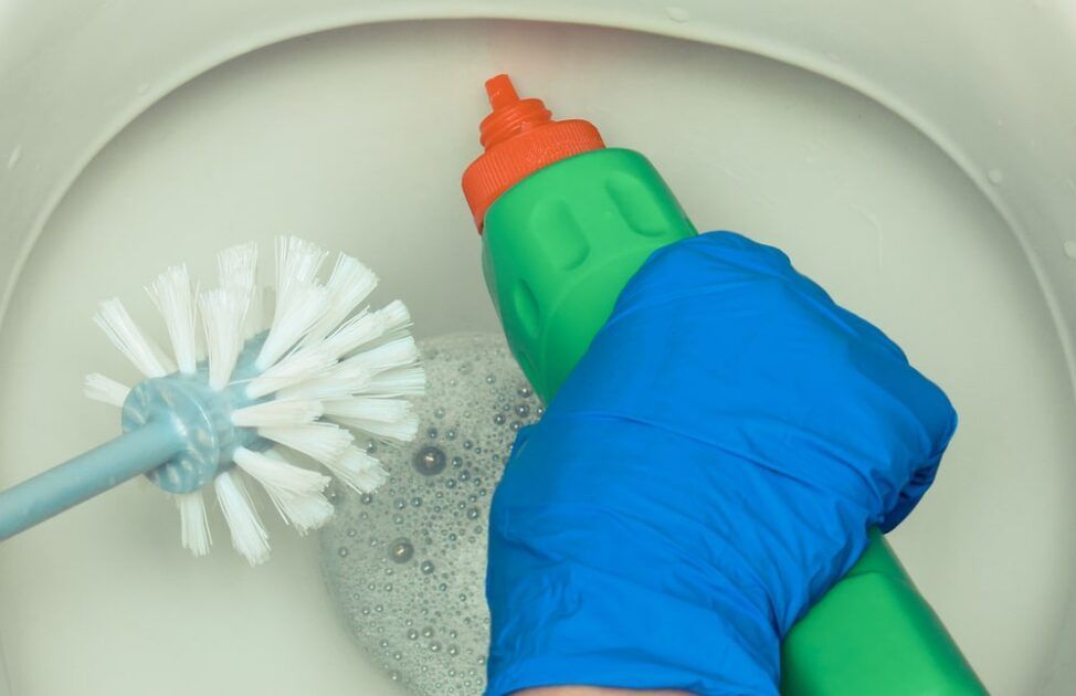 A person is cleaning a toilet with a brush and a bottle of cleaner.