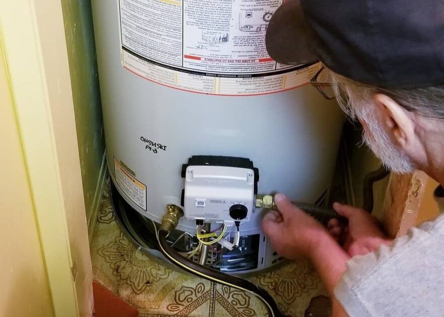 A man is fixing a water heater with a wrench.