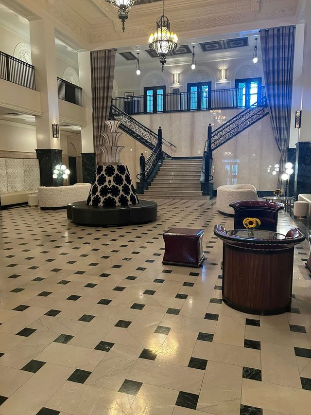 Grand hotel lobby with marble floors, chandelier, grand staircase, and central seating area
