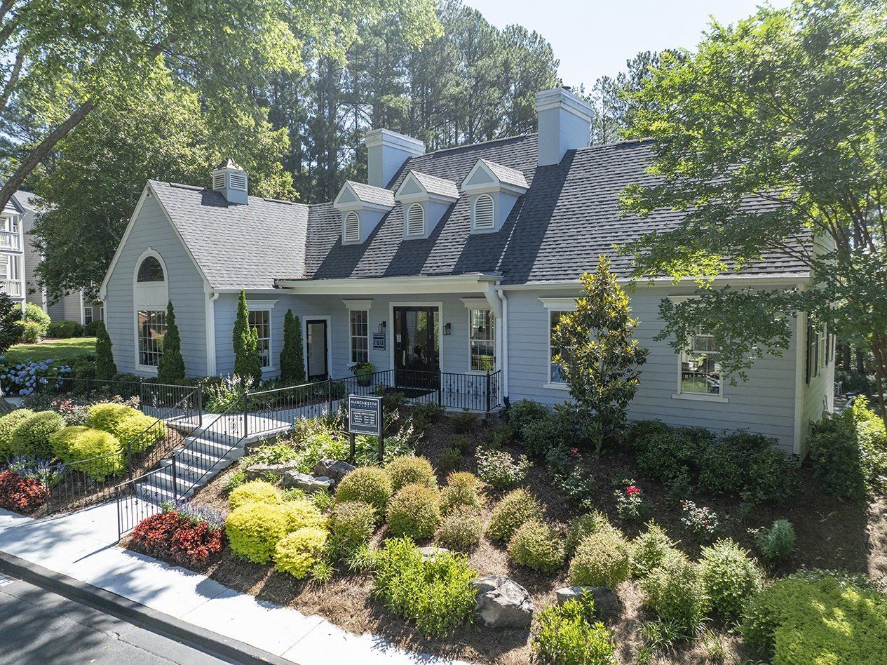 A light blue building with a dark roof and a well-manicured garden under a sunny sky at Man