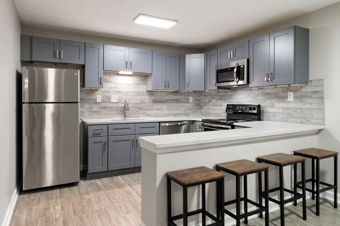 Modern kitchen with gray cabinets, stainless steel appliances, and a breakfast bar with stools.