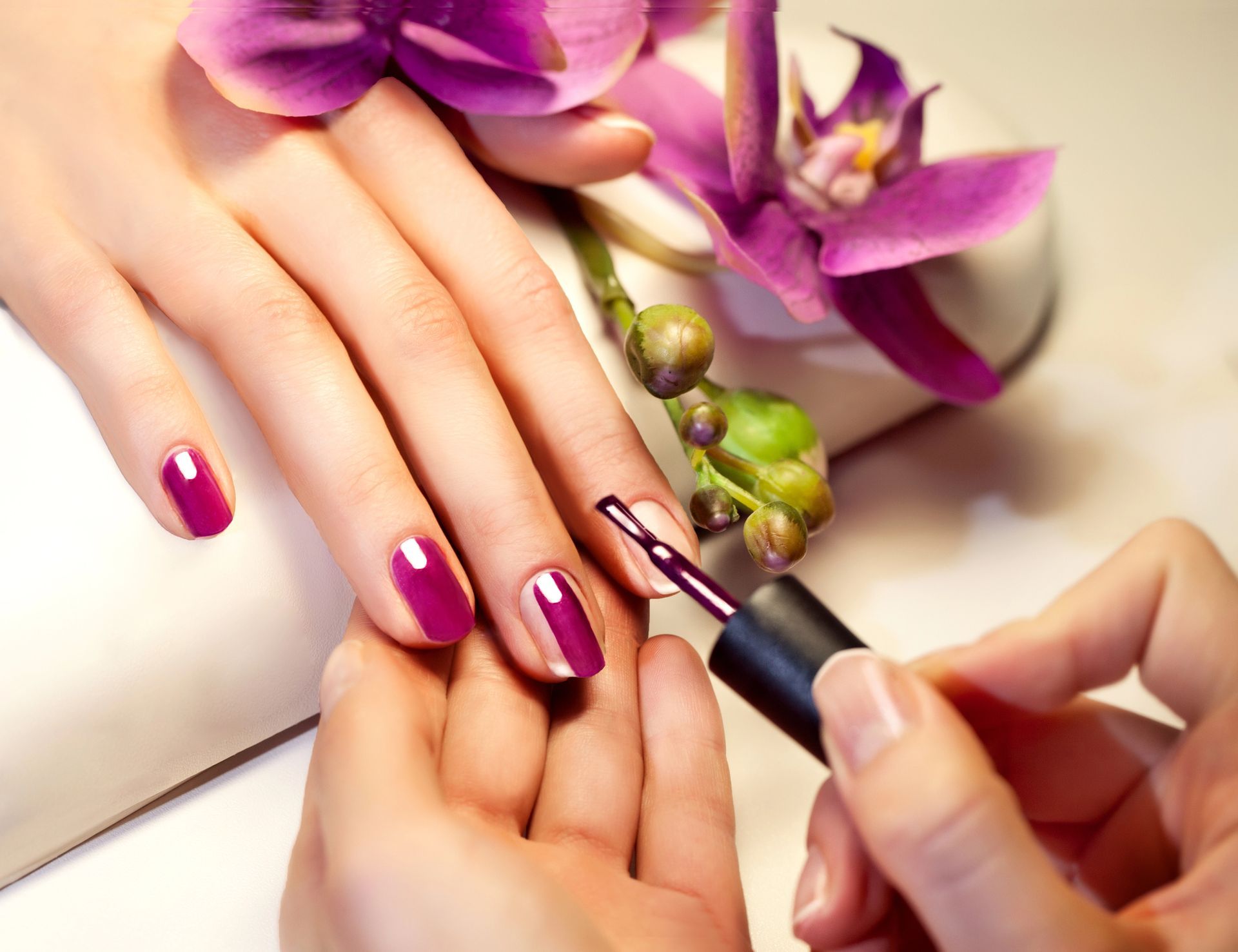 Unghie curate e dipinte di rosa intenso mentre un'estetista applica lo smalto, con fiori viola nelle vicinanze.
