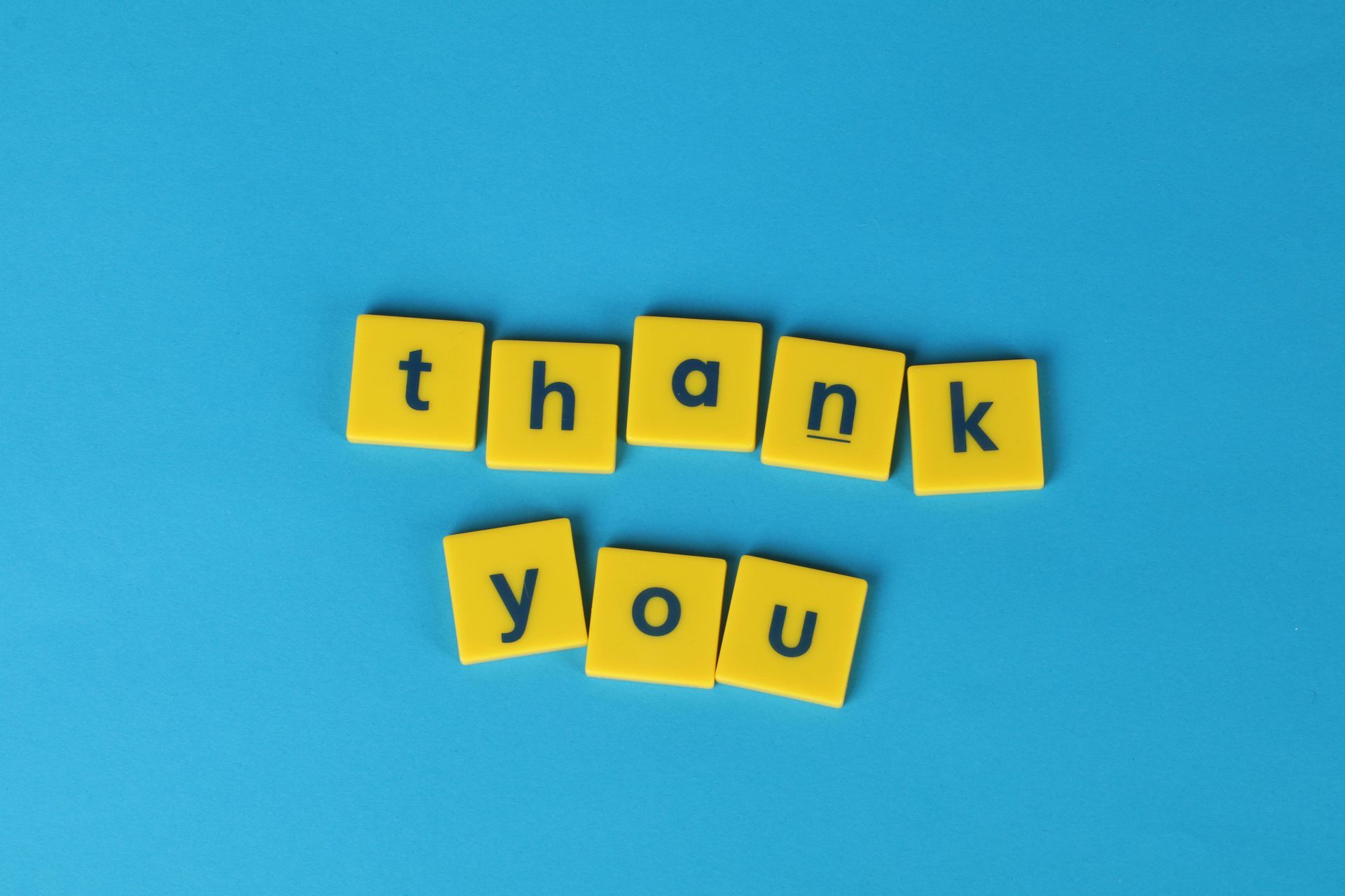 The word thank you is written in yellow scrabble tiles on a blue background.