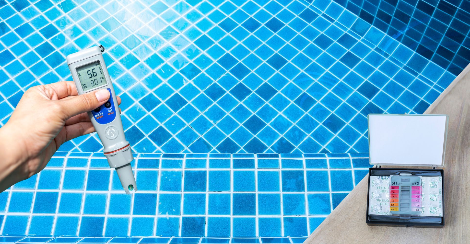 A person is holding a thermometer in front of a swimming pool.