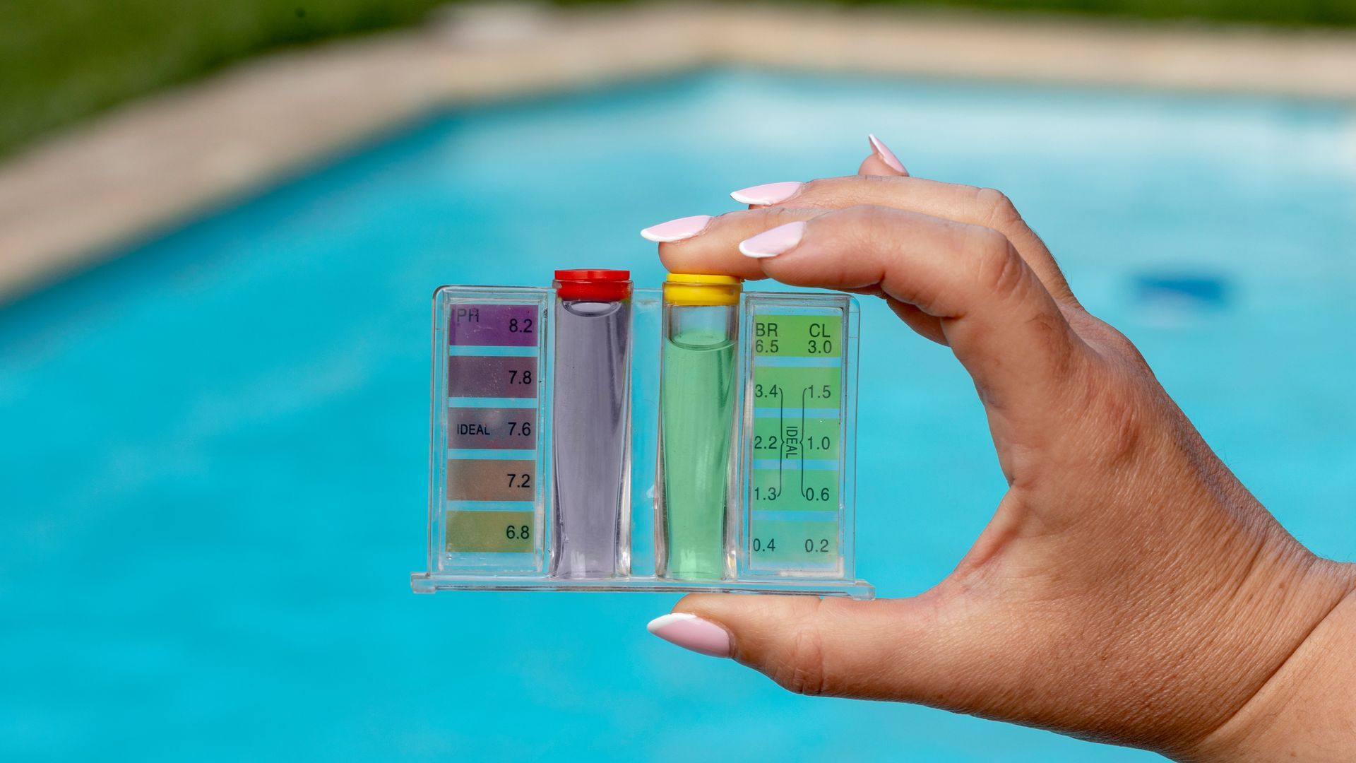 A person is holding a test tube in front of a swimming pool.
