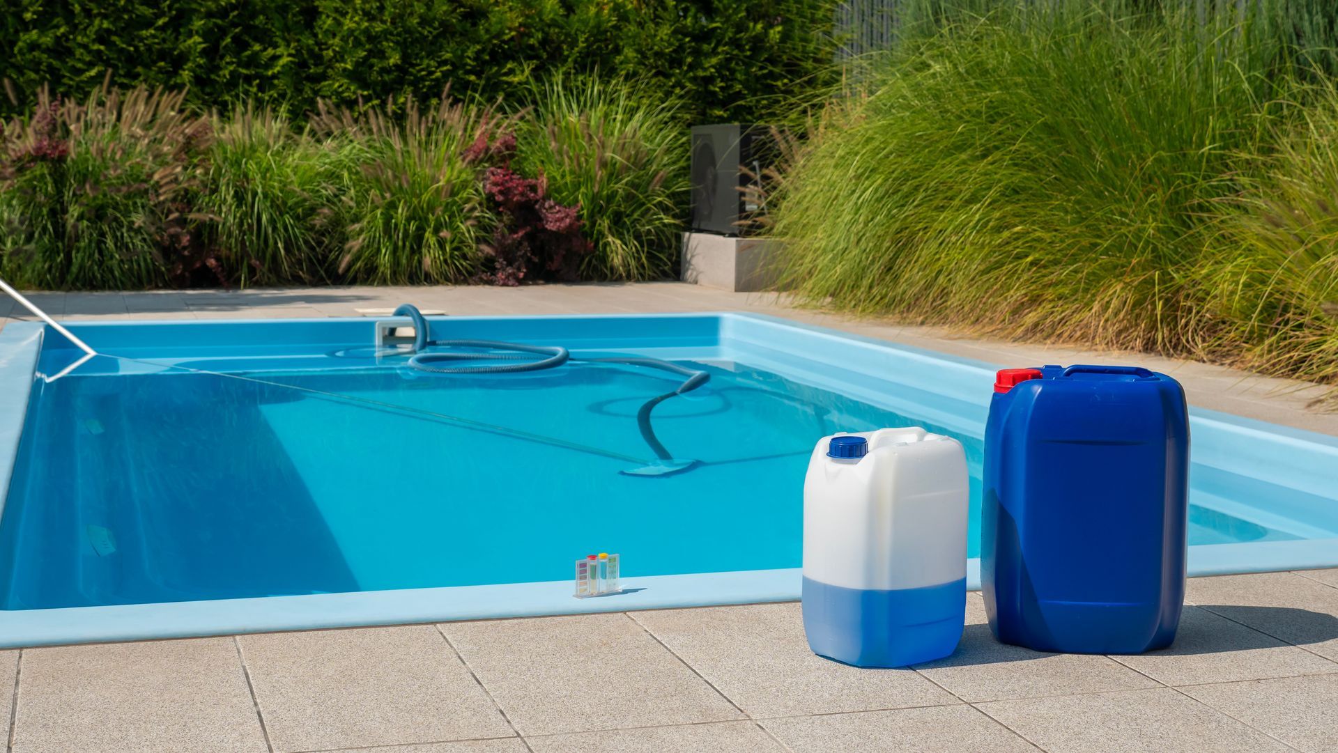 Two cans of chemicals are sitting next to a swimming pool.
