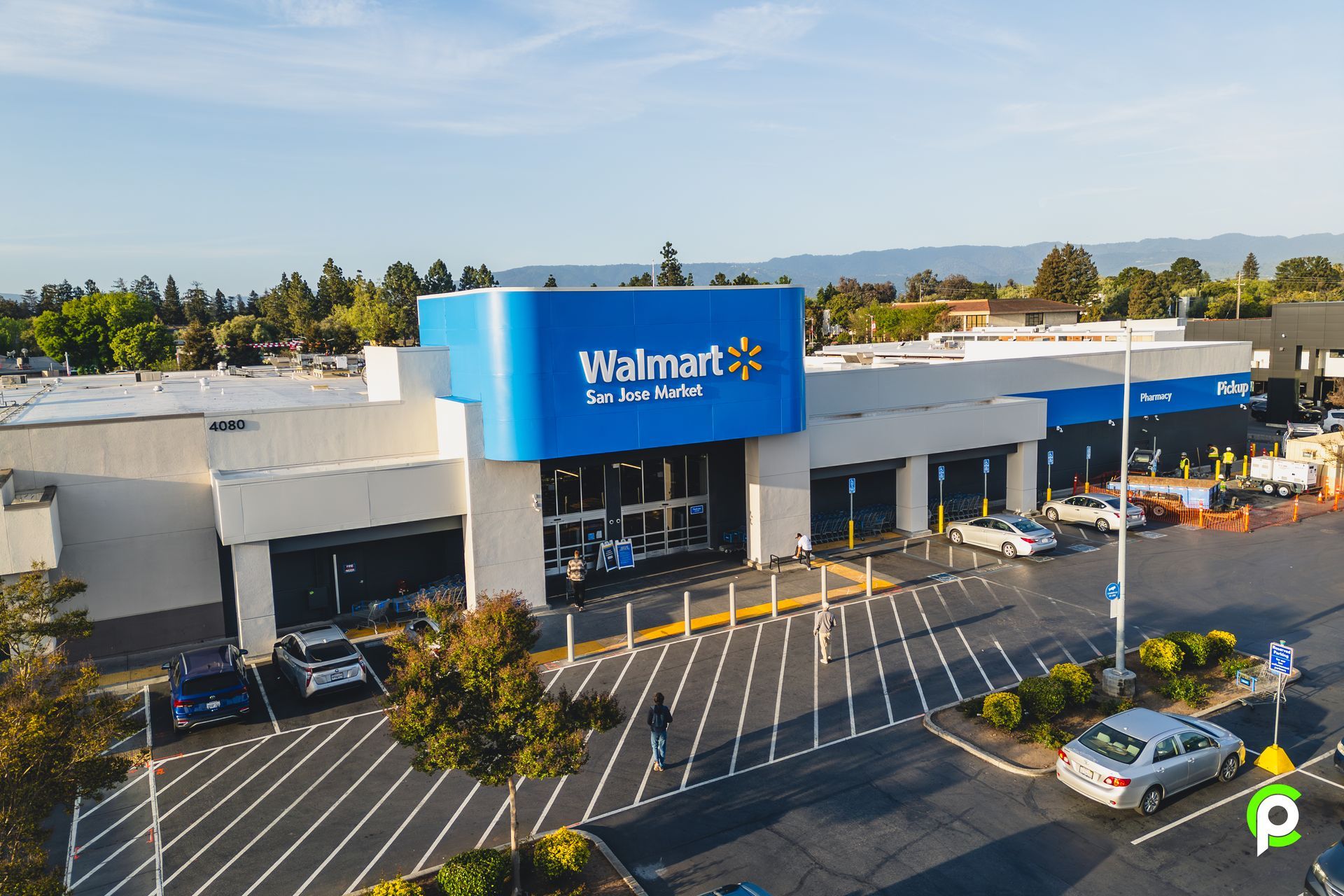 Aerial view of a Walmart store with blue signage, parking lot with cars, and trees.
