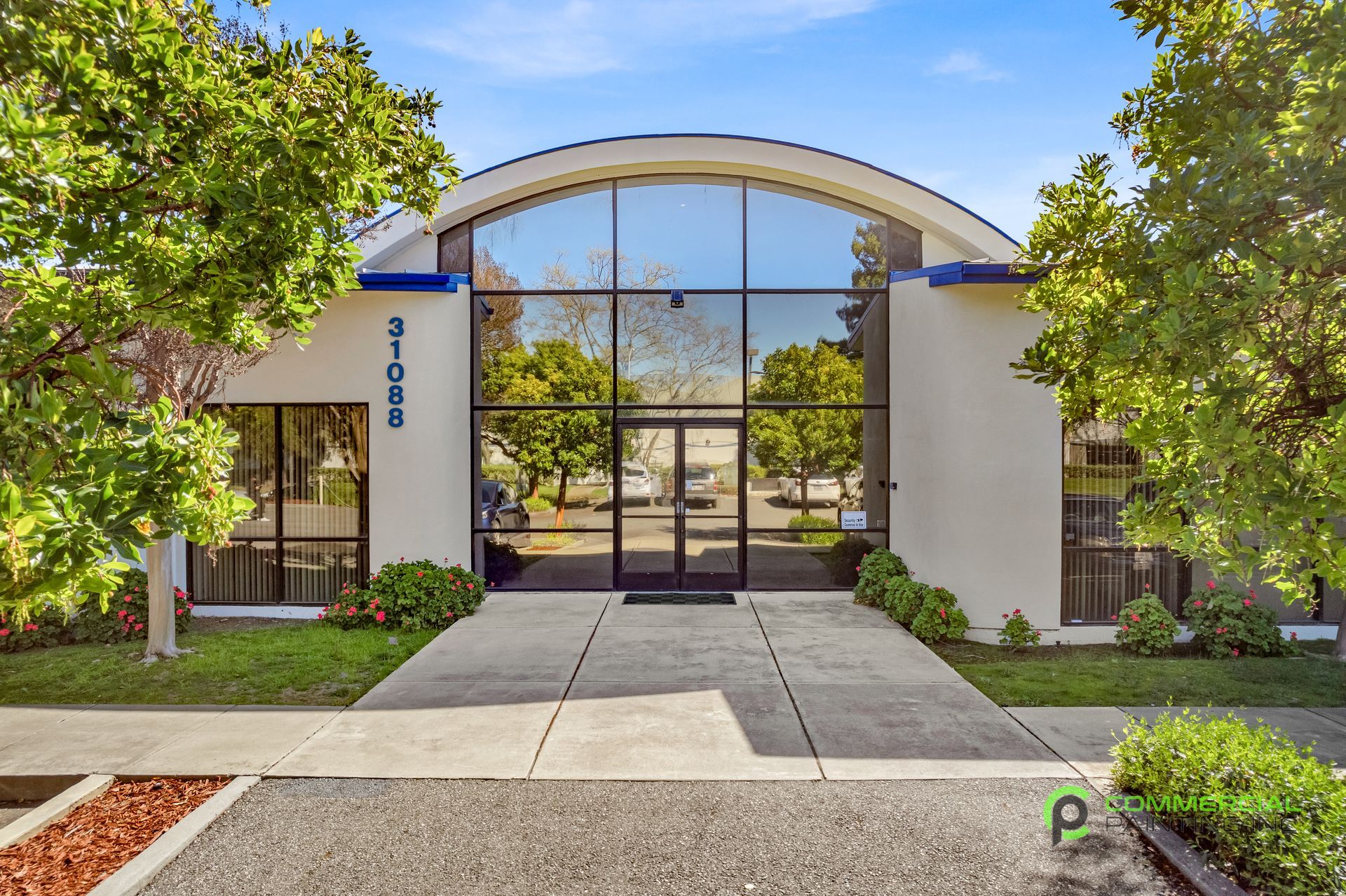 Office building with large glass windows and arched top. Exterior is white, with trees and greenery in front.
