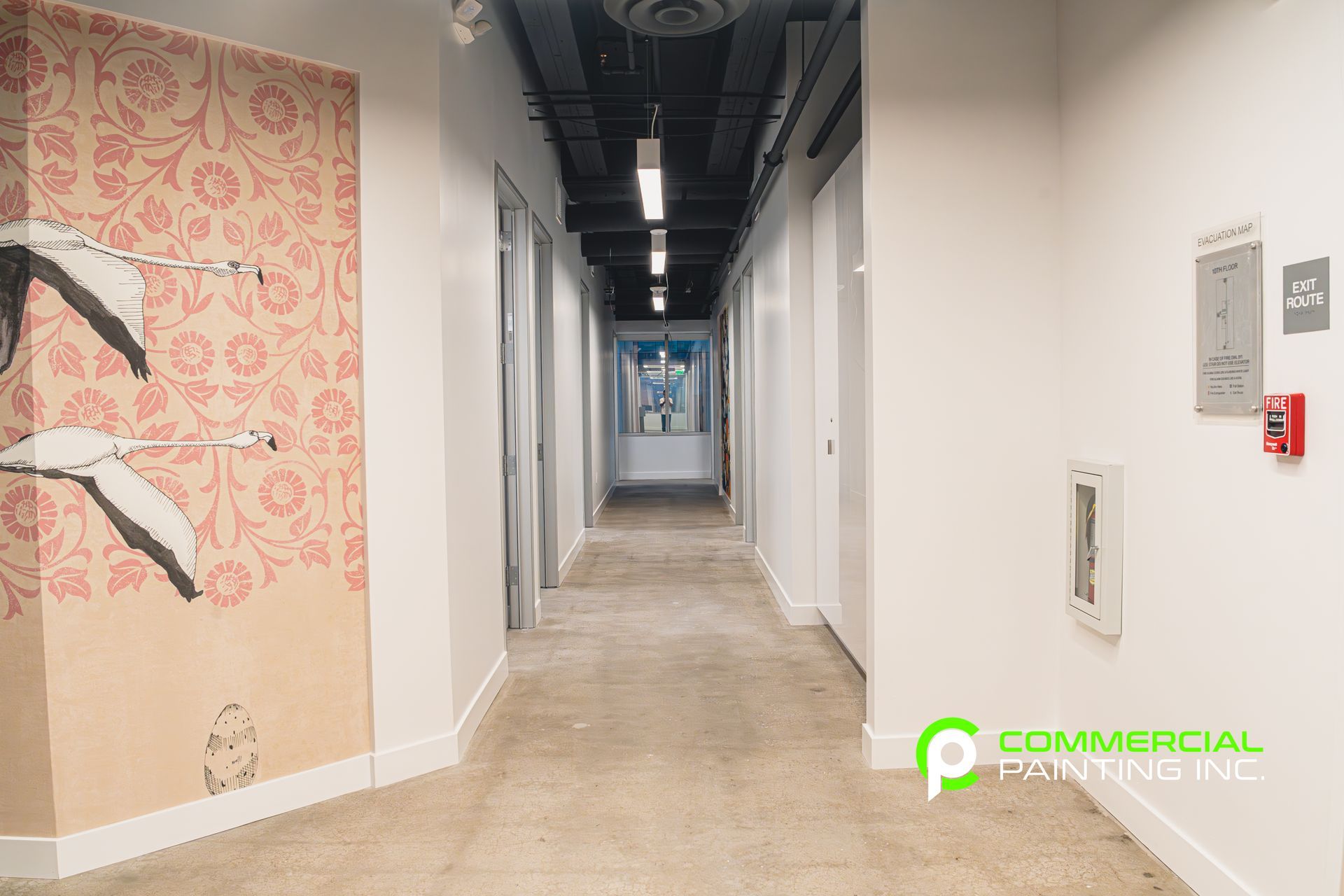 A hallway with a painting on the wall and a fire alarm.