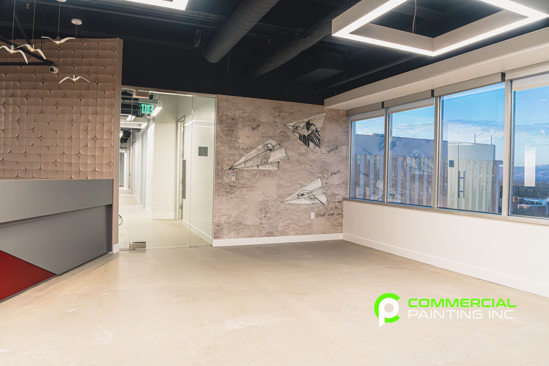 A large empty room with a lot of windows and a painting on the wall.