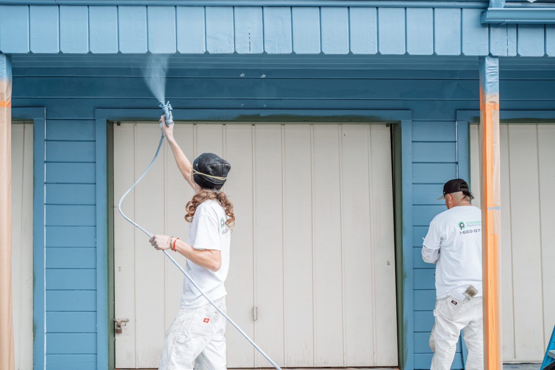 A man and a woman are painting a blue house.
