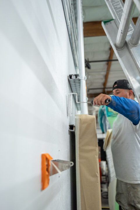 A man is painting a wall with a ladder in the background.