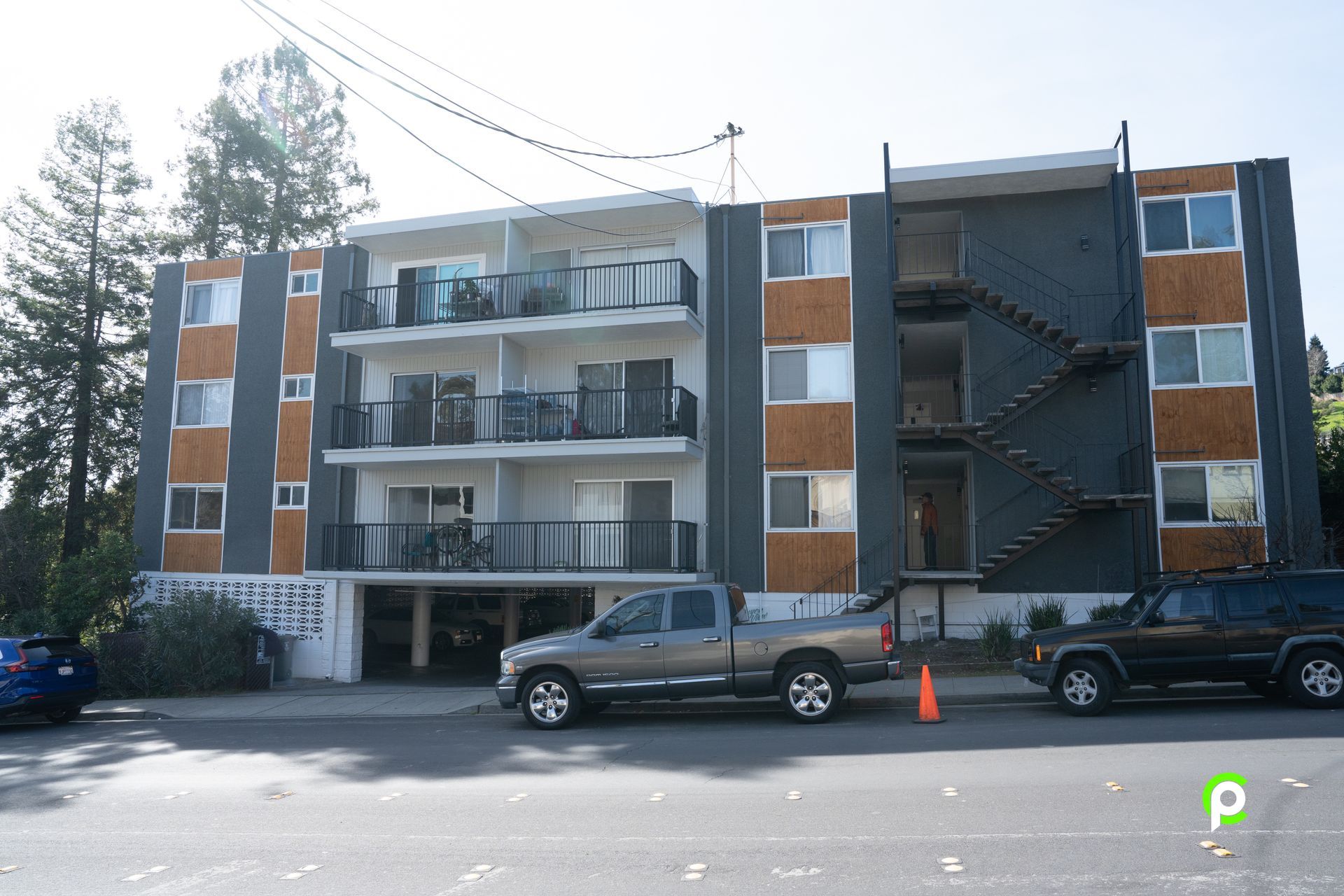 A gray truck is parked in front of a large apartment building.