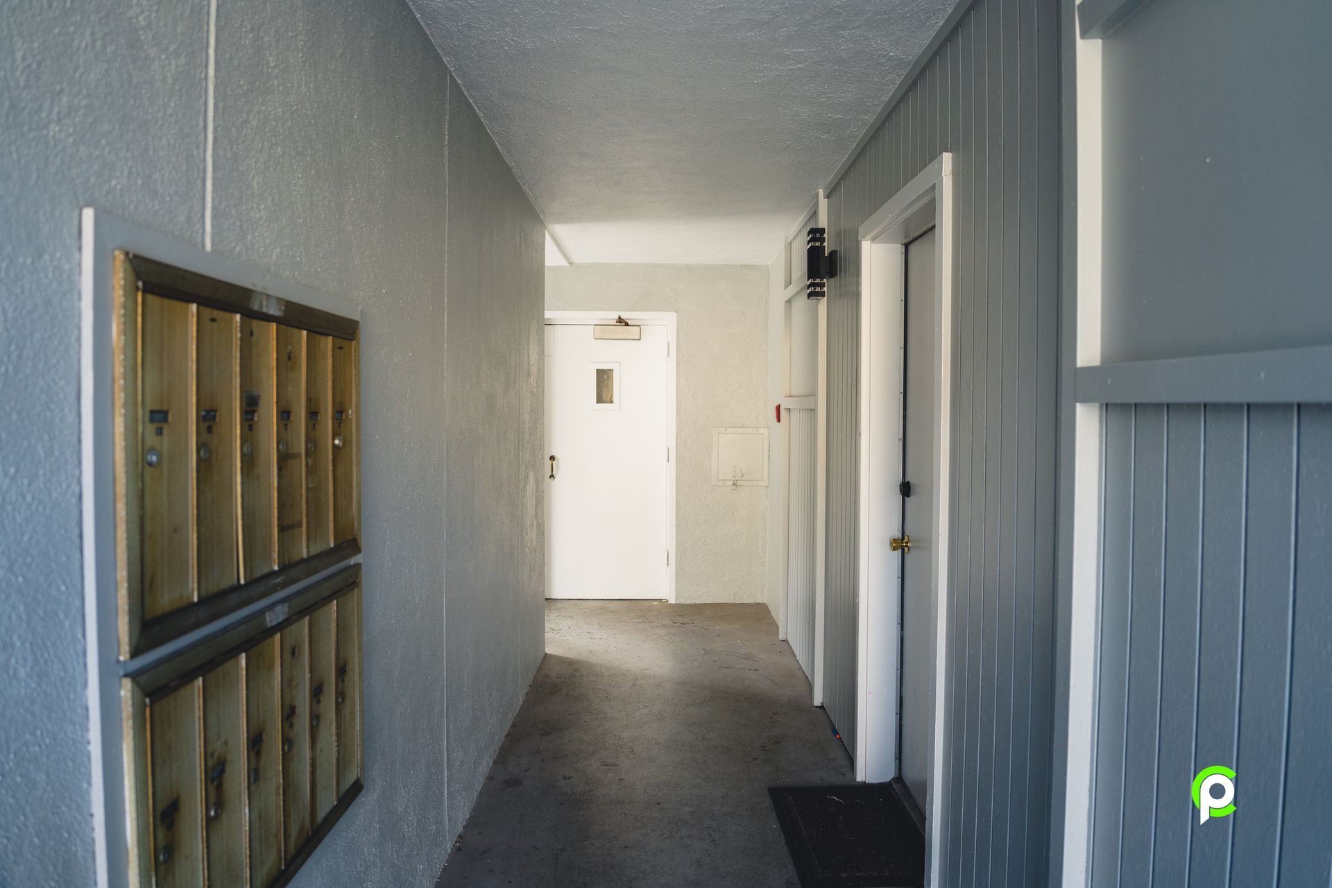 A hallway with a door and mailboxes on the wall.