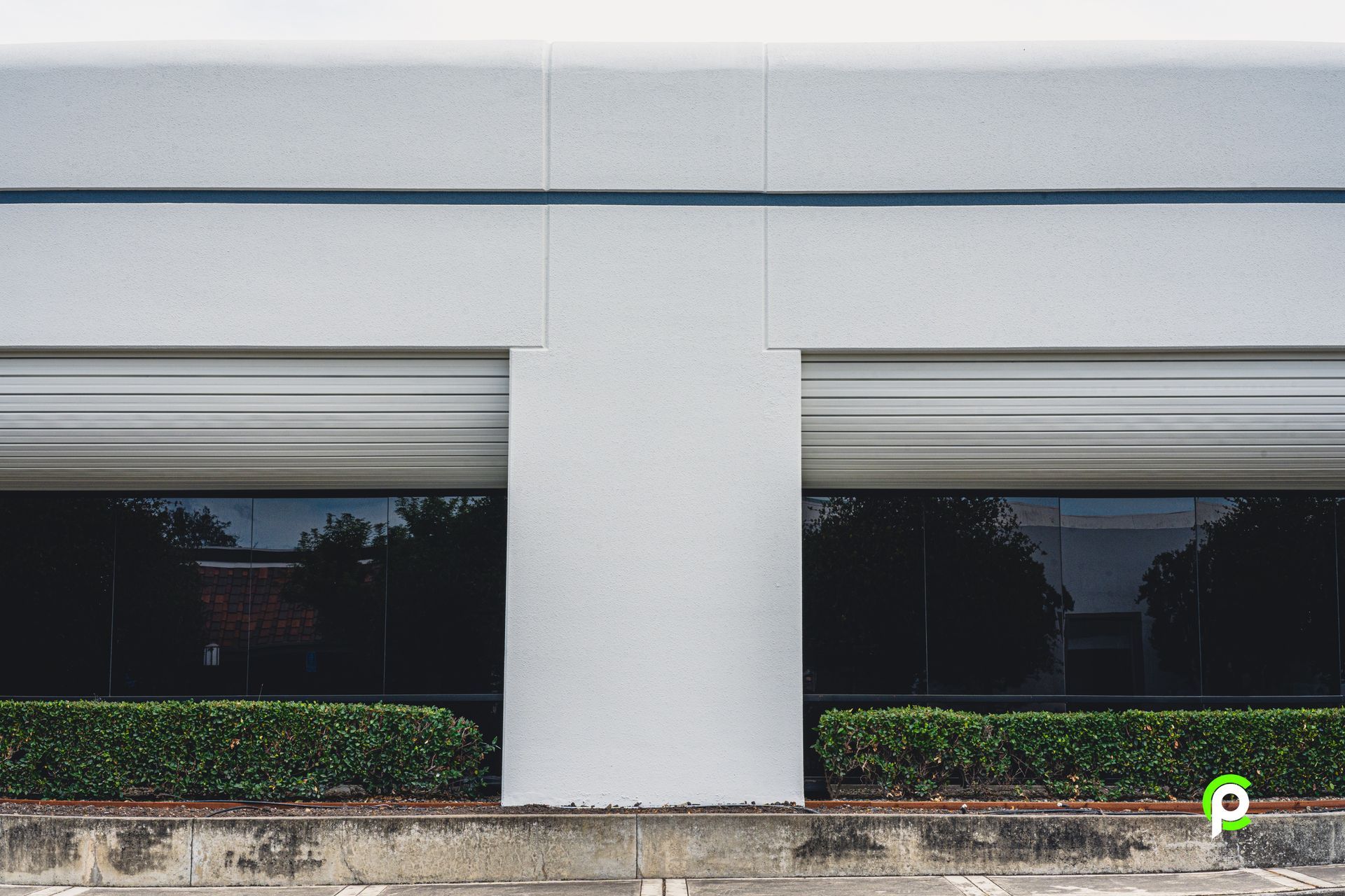 A white building with a lot of windows and bushes in front of it.
