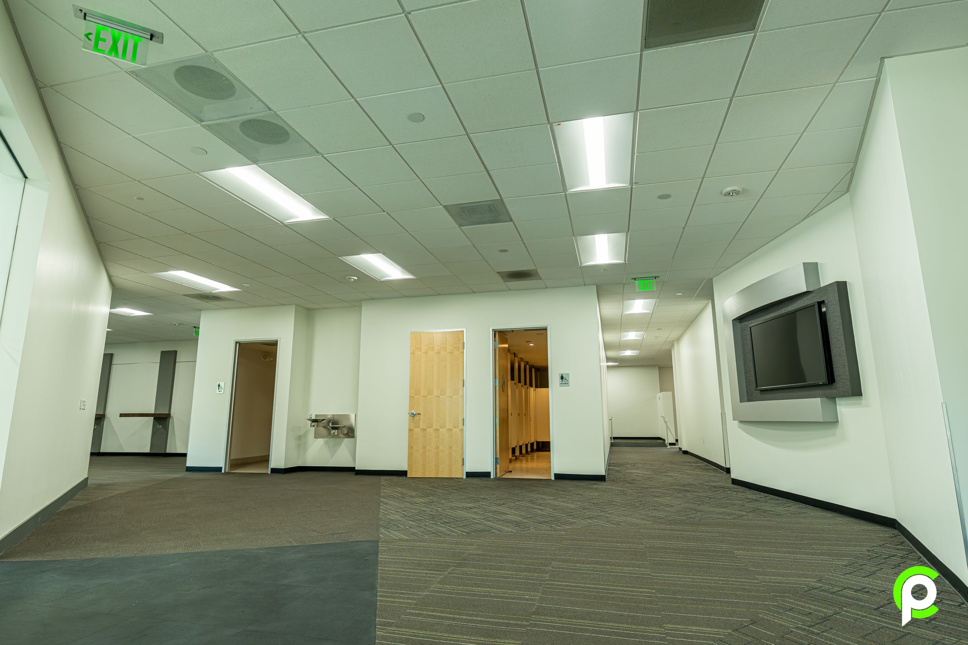 A large empty room with a green exit sign on the ceiling.