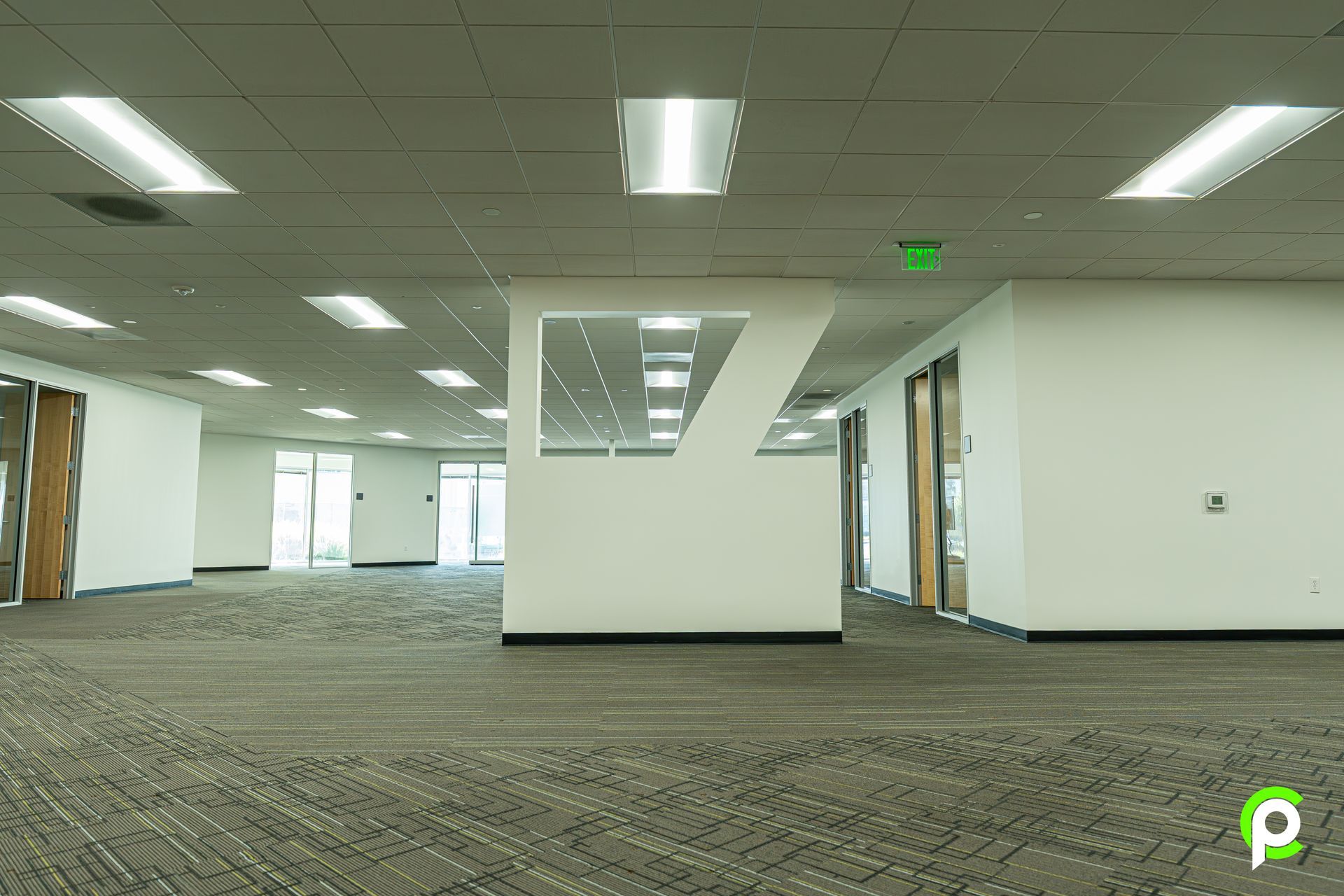 A large empty room with a green exit sign on the ceiling