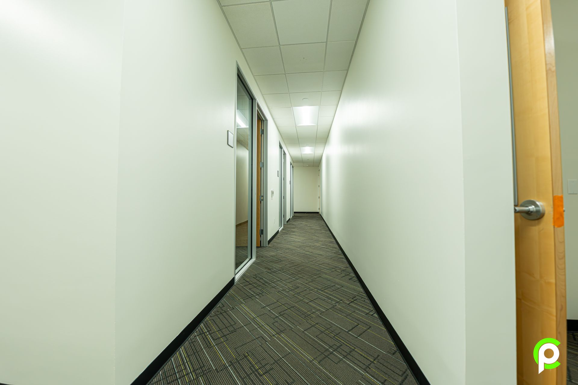 A long hallway in an office building with white walls and a brown carpet.