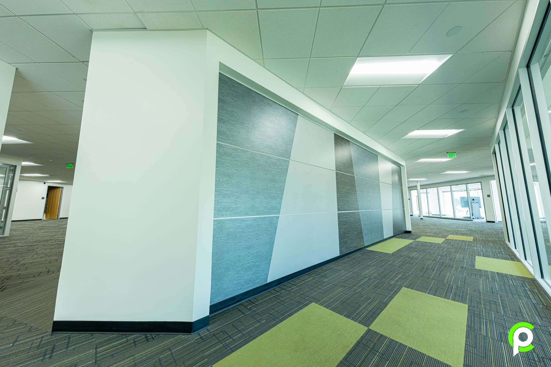 A long hallway in an office building with green carpet and white walls.