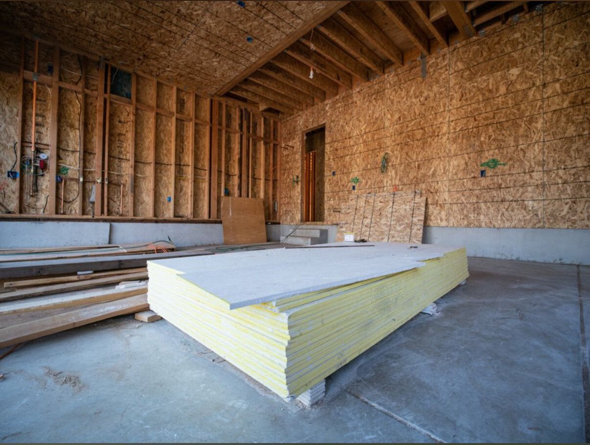 Interior of a garage under construction, with a stack of drywall sheets.