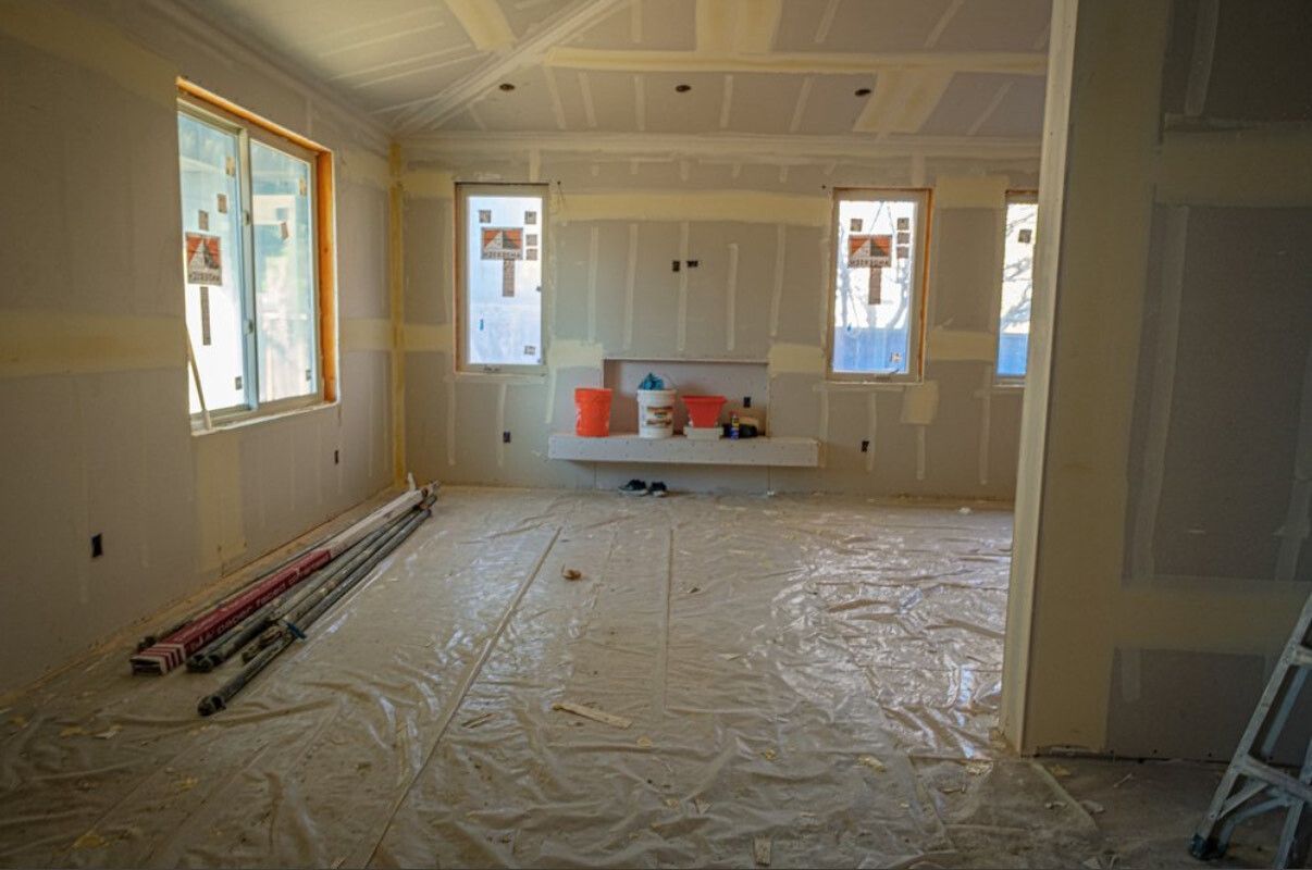Interior room under construction, drywall, windows, plastic floor covering, building materials, unfinished.