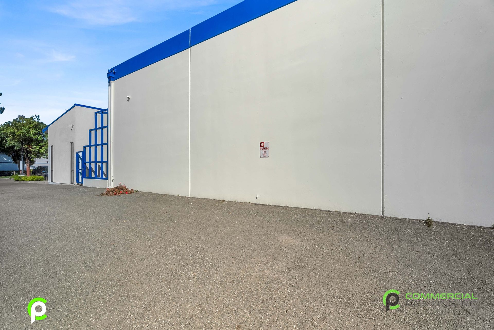 A white building with a blue trim is sitting next to a gravel road.
