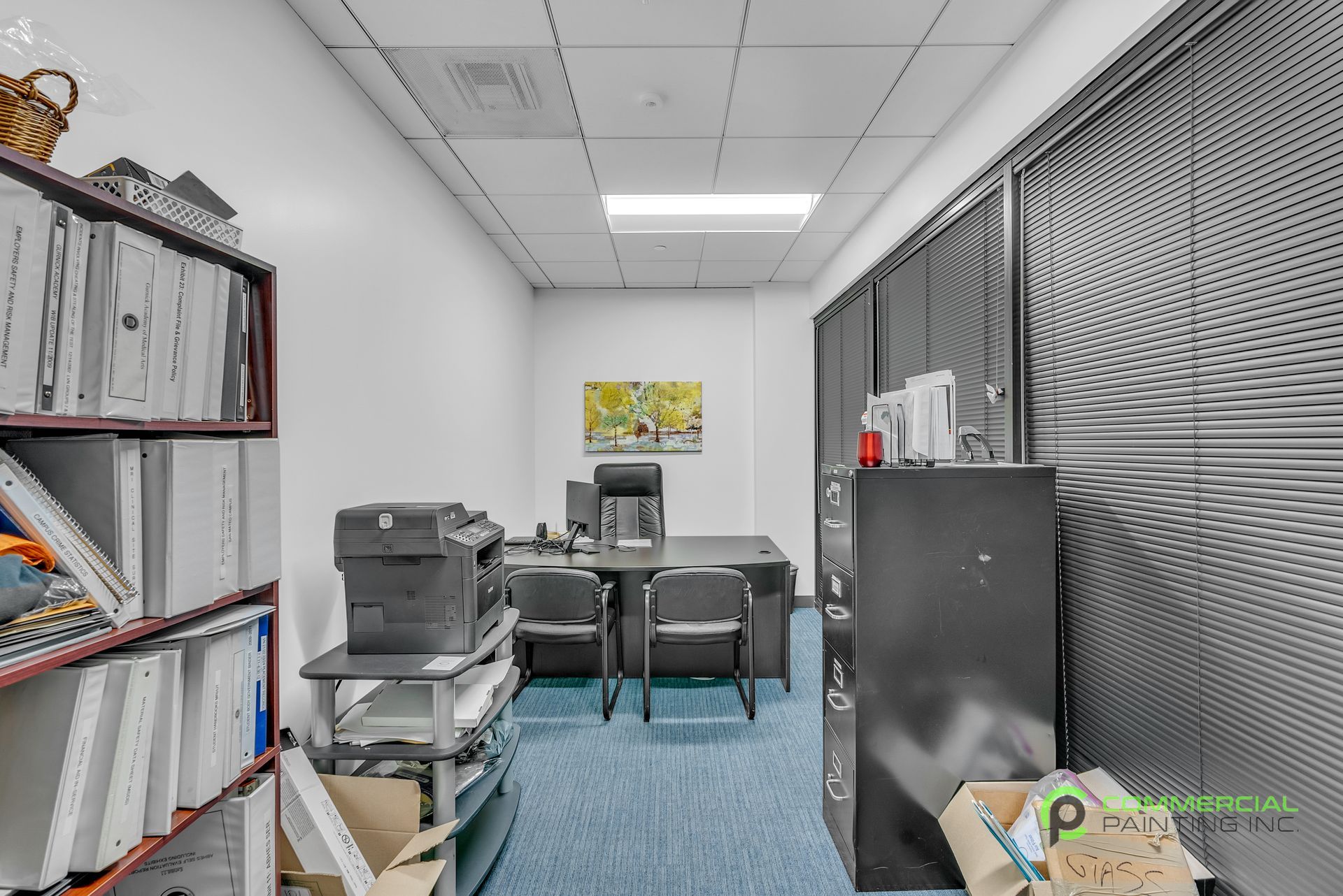 A small office with a desk , chairs , shelves and a printer.