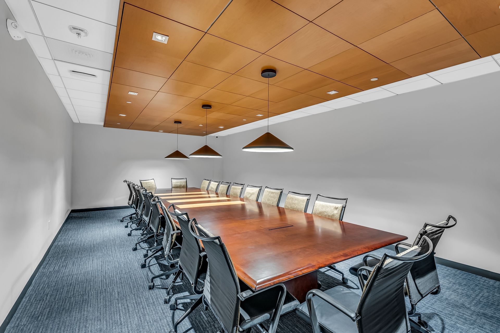 Conference room with large wooden table, chairs, and wood-paneled ceiling.