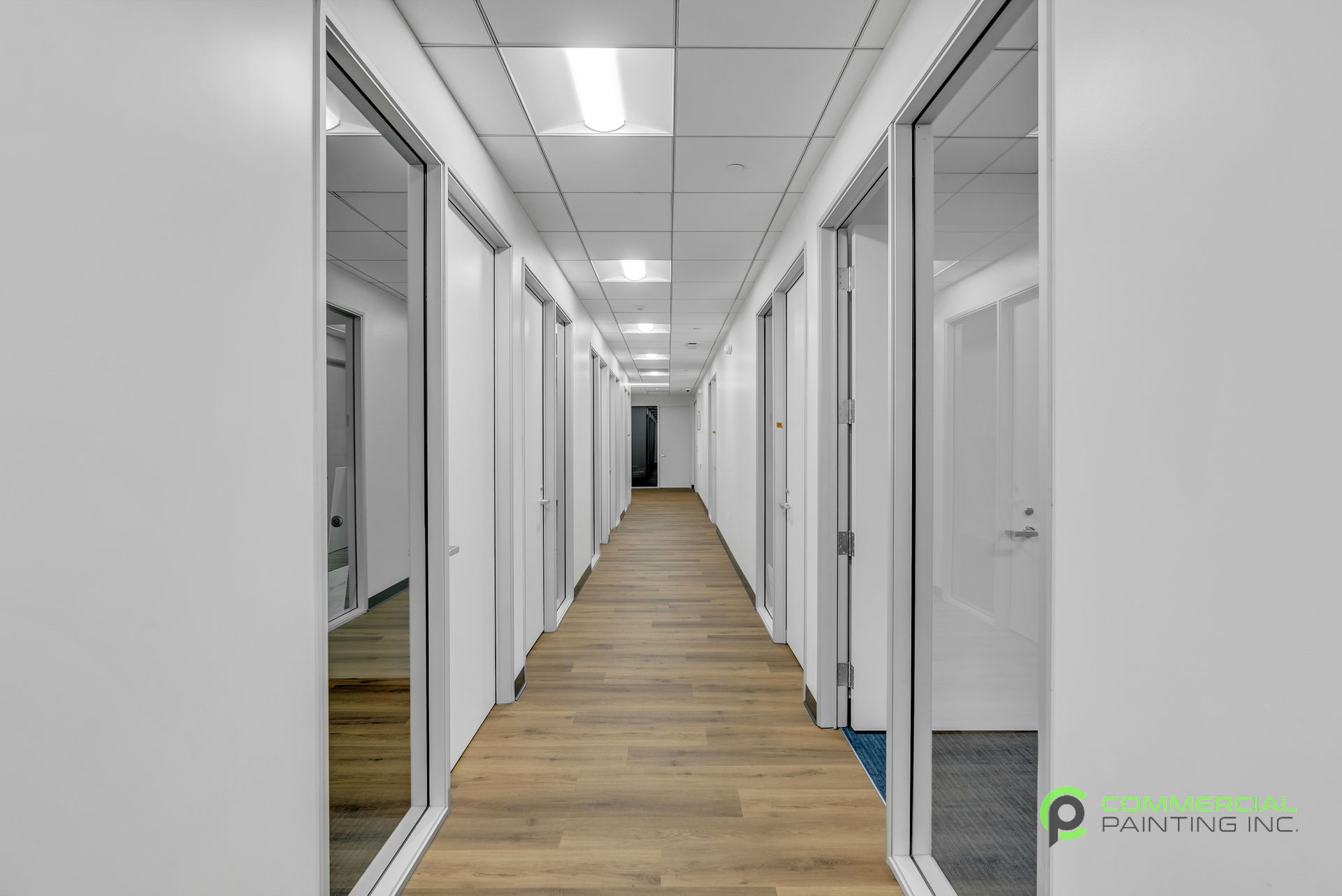 A long hallway in an office building with wooden floors and white walls.