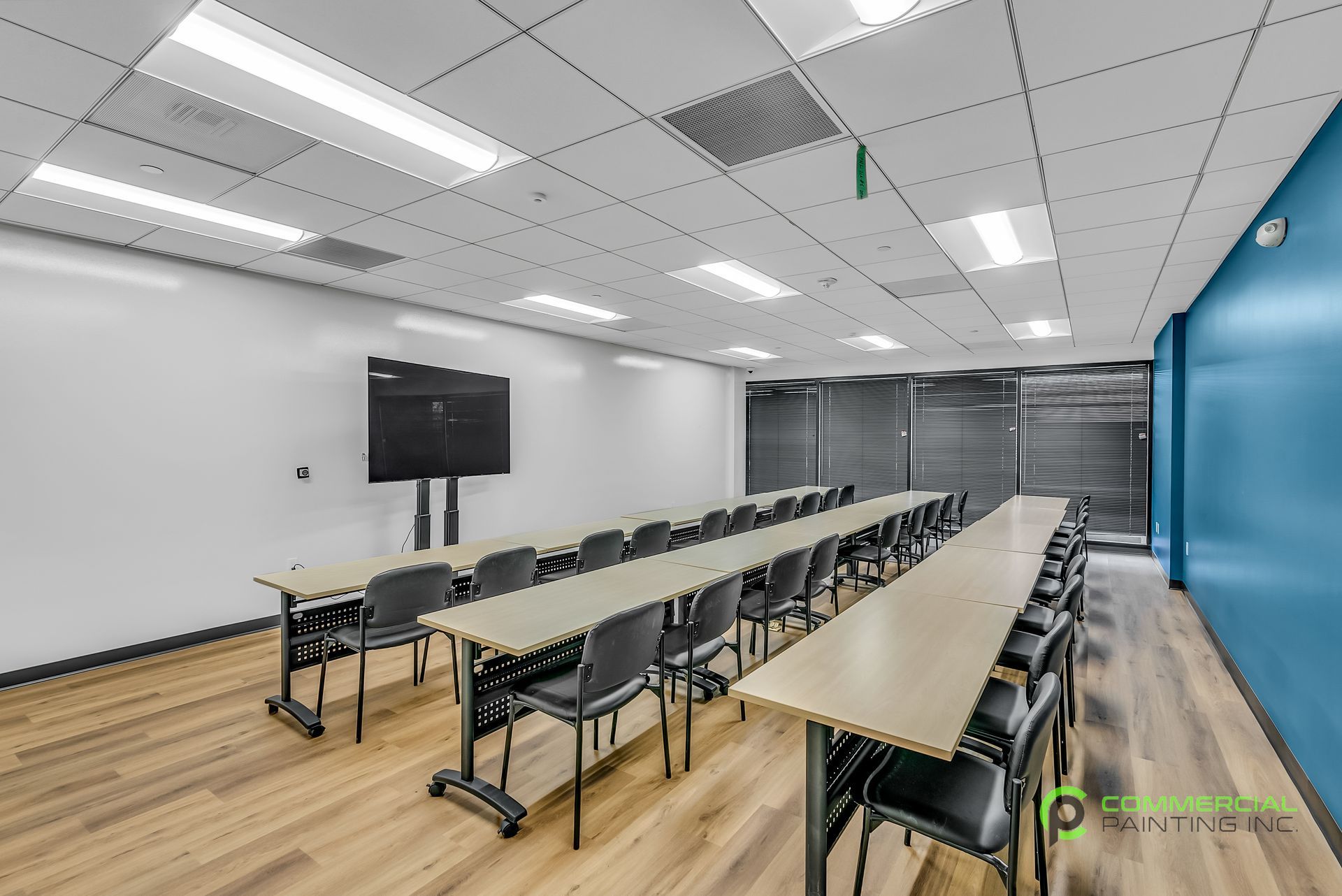 A large conference room with tables and chairs and a flat screen tv on the wall.