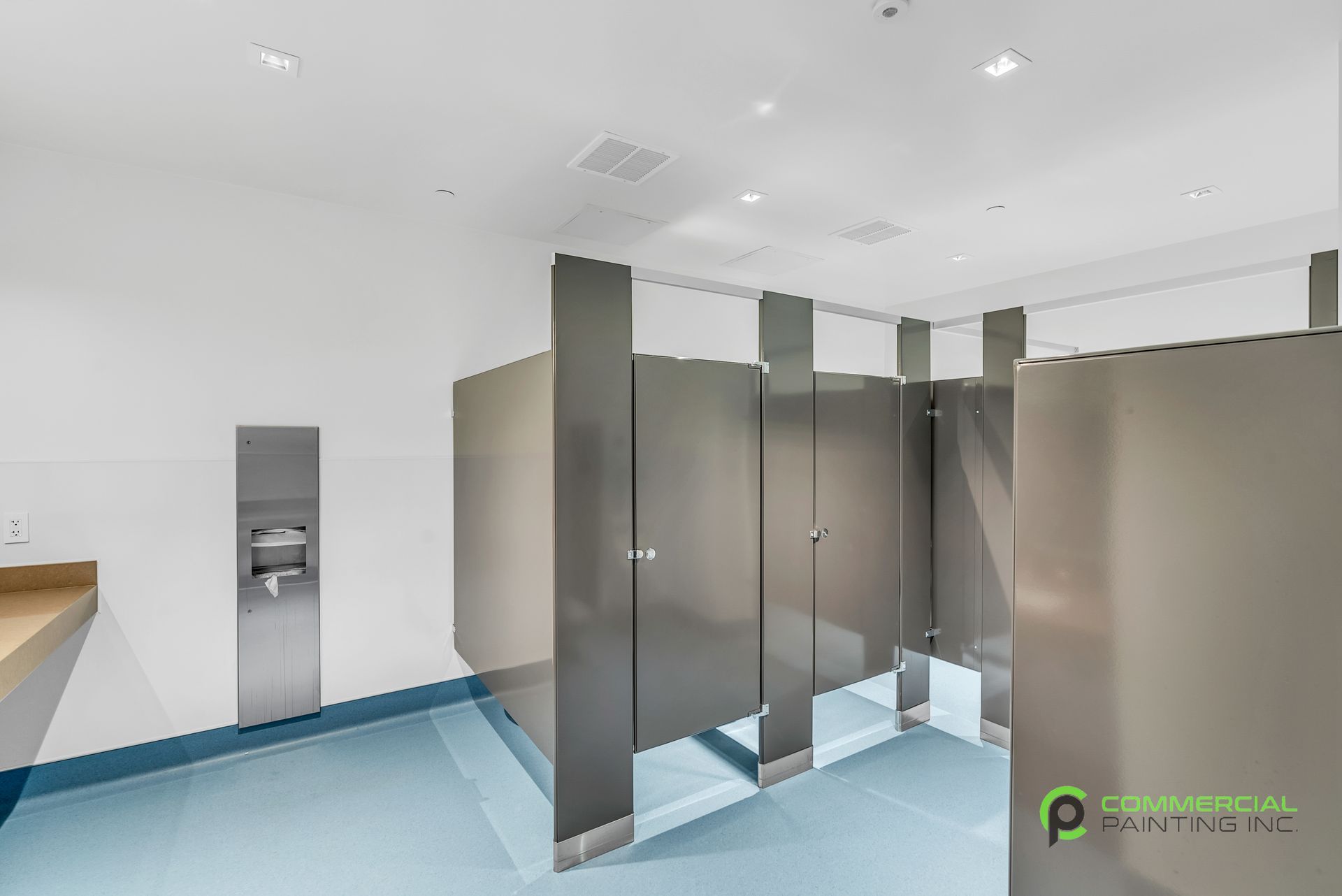 A public restroom with stainless steel stalls and a blue floor.