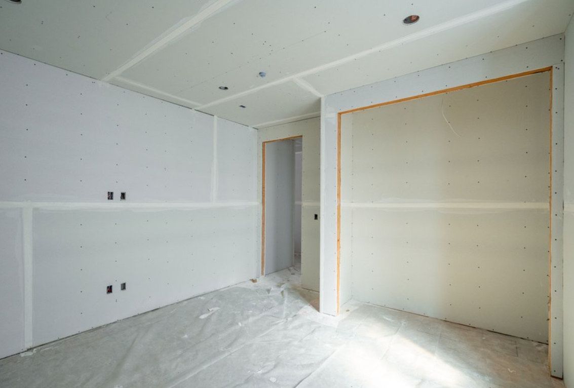 Interior of a room under construction with drywall installed on walls and ceiling.
