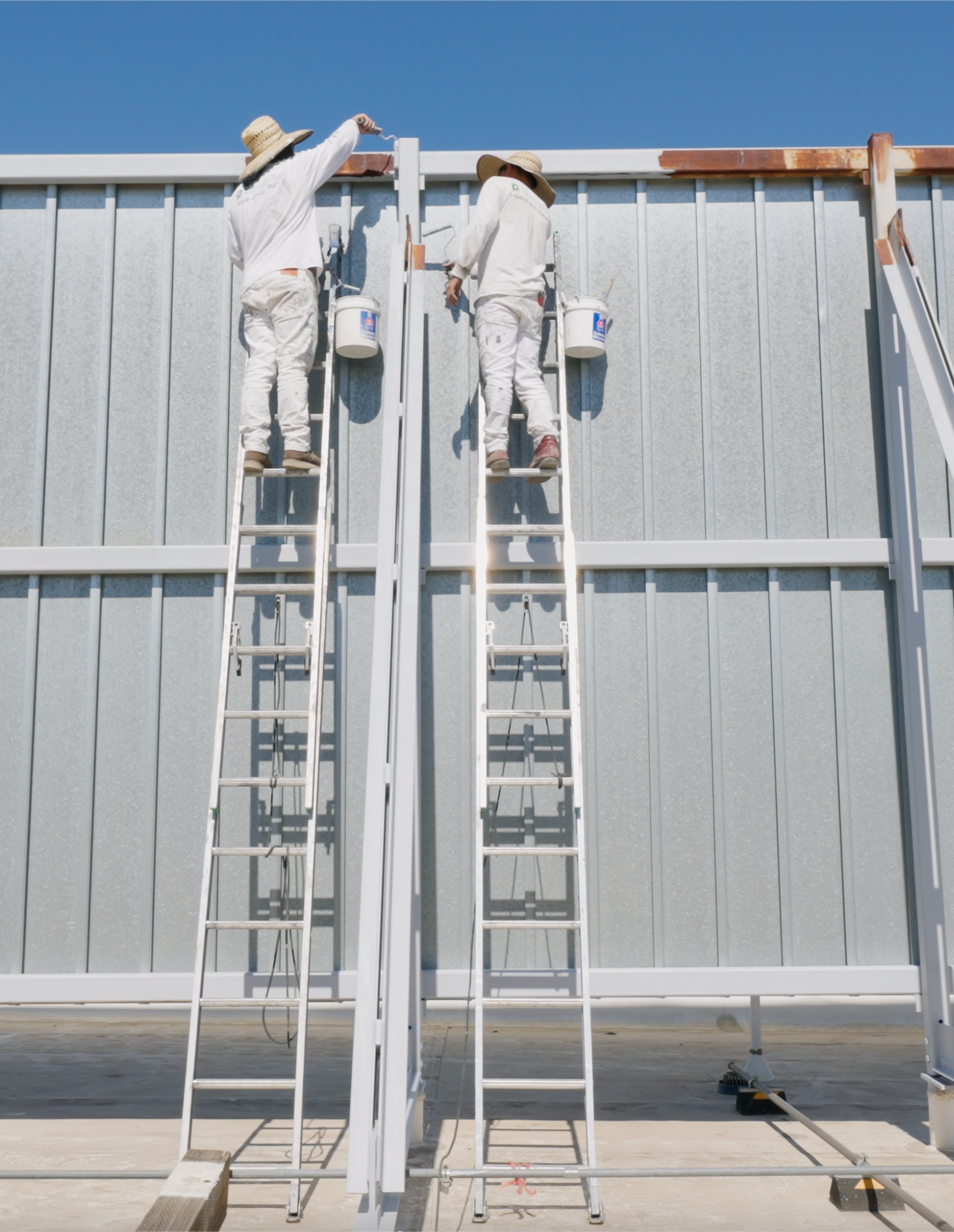 Person in protective suit sprays paint on metal structure.