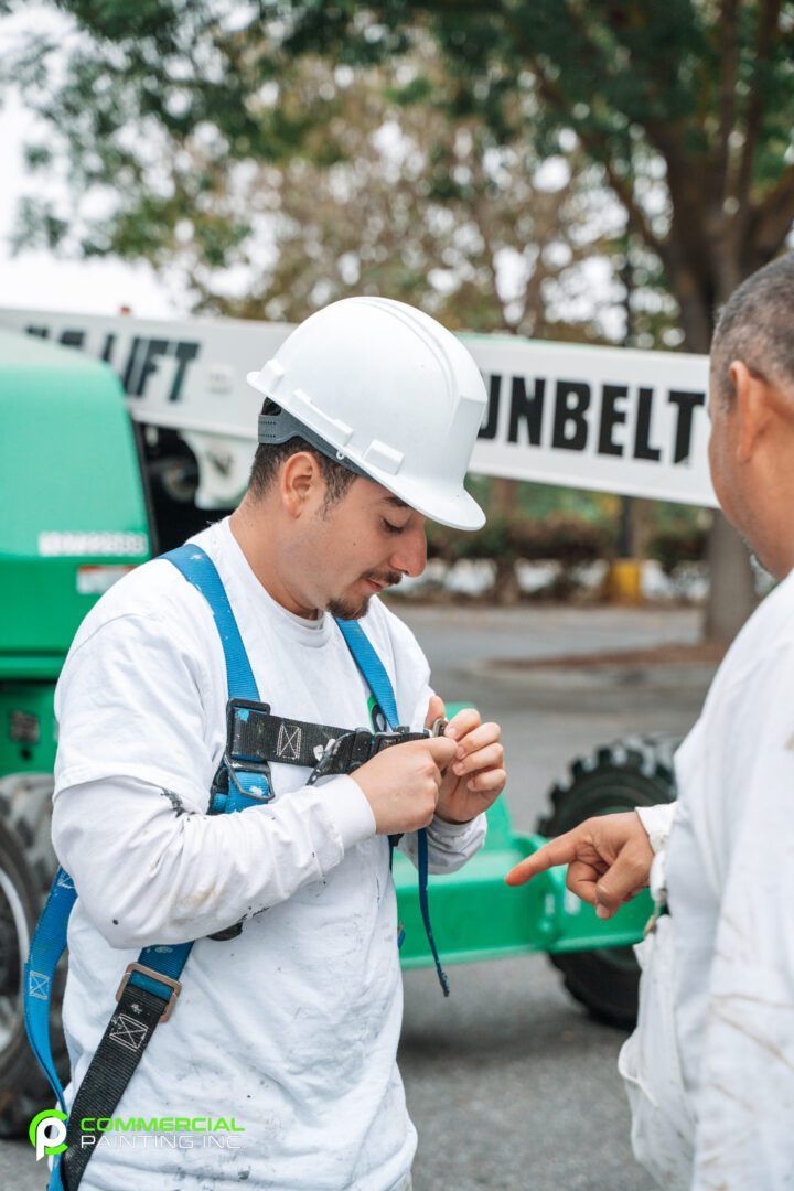 A man wearing a hard hat and safety harness is talking to another man.