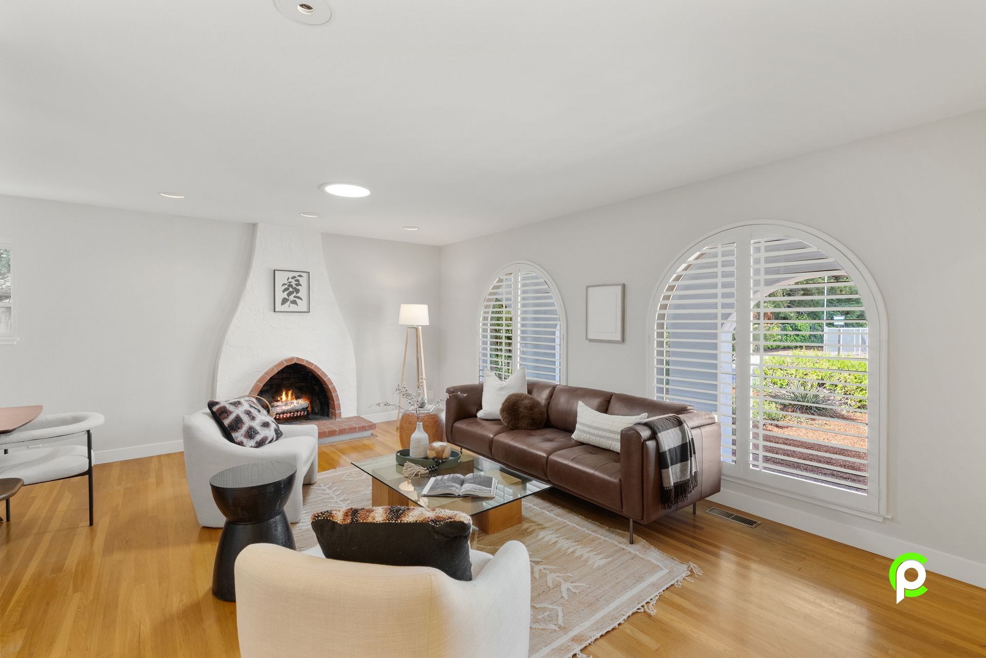 Living room with a fireplace, leather sofa, arched windows, and hardwood floors.